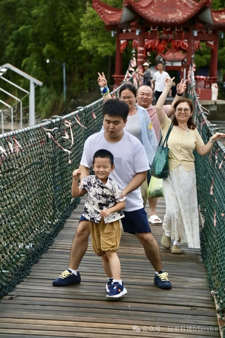 同事带着孩子走过千岛湖景区索桥，桥头是红色亭子，一家人比出胜利手势