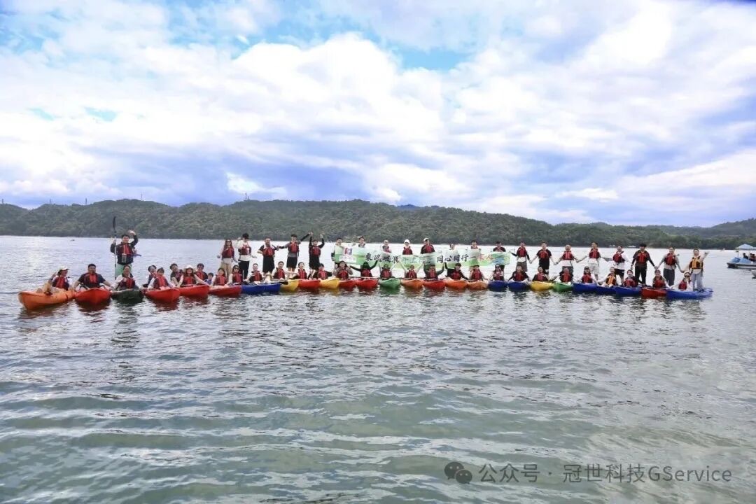 冠世科技团队十余条彩色皮划艇在千岛湖湖面首尾相连排成一线，众人举手合影，背景是蓝天白云与青山