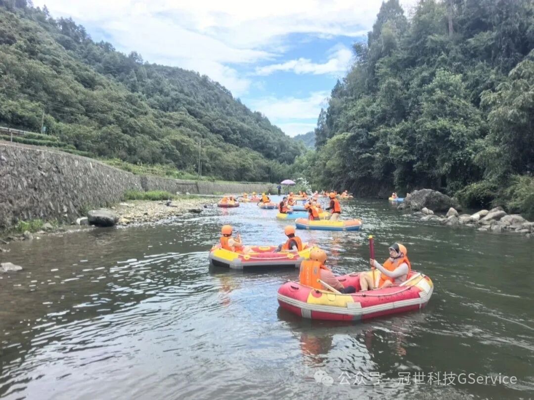 同事乘坐橡皮筏在山谷溪流中漂流，两岸树木葱郁，天空湛蓝