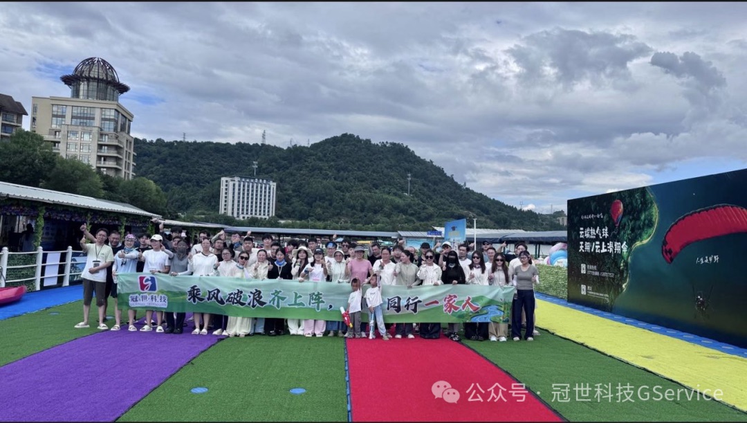 冠世科技全体员工及家属在千岛湖水上乐园彩色草坪合影，手持「乘风破浪齐上阵，同心同行一家人」横幅